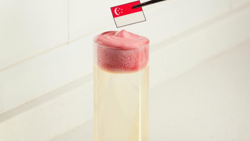 Nutmeg & Clove bartender garnishing a pink cocktail with a Singapore flag pick at the bar counter